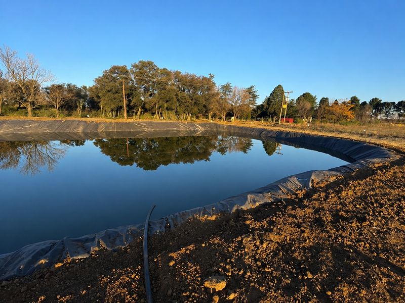 A large lined agricultural reservoir or dam situated on the small holding, featuring clear water and surrounding natural landscape.