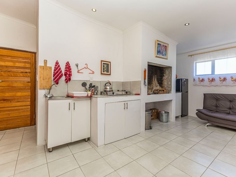 Open plan living area featuring a kitchenette with built-in cabinetry, hob, sink, and a traditional built-in fireplace with tiled flooring throughout.