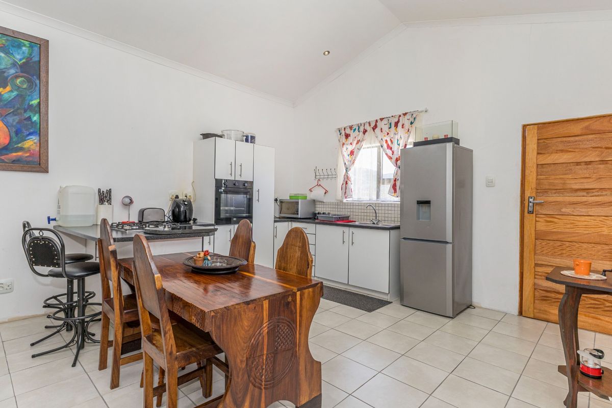 A functional kitchen featuring white cabinetry, built-in oven, hob, and tiled flooring, with a vaulted ceiling and direct access to the dining area.