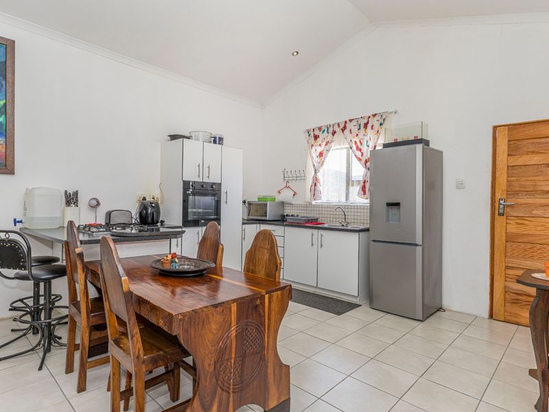 A functional kitchen featuring white cabinetry, built-in oven, hob, and tiled flooring, with a vaulted ceiling and direct access to the dining area.
