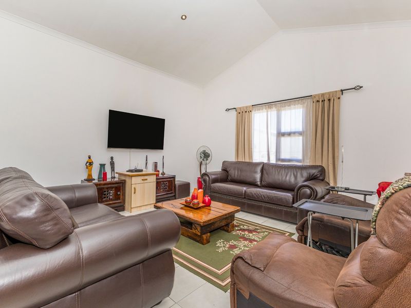 Spacious living room featuring a high vaulted ceiling, neutral tiled flooring, and large window with curtain fixtures.