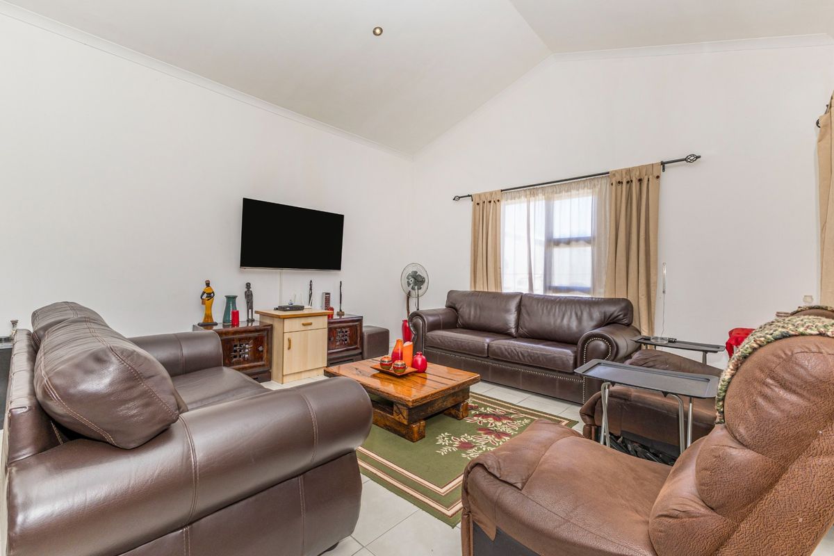 Spacious living room featuring a high vaulted ceiling, neutral tiled flooring, and large window with curtain fixtures.