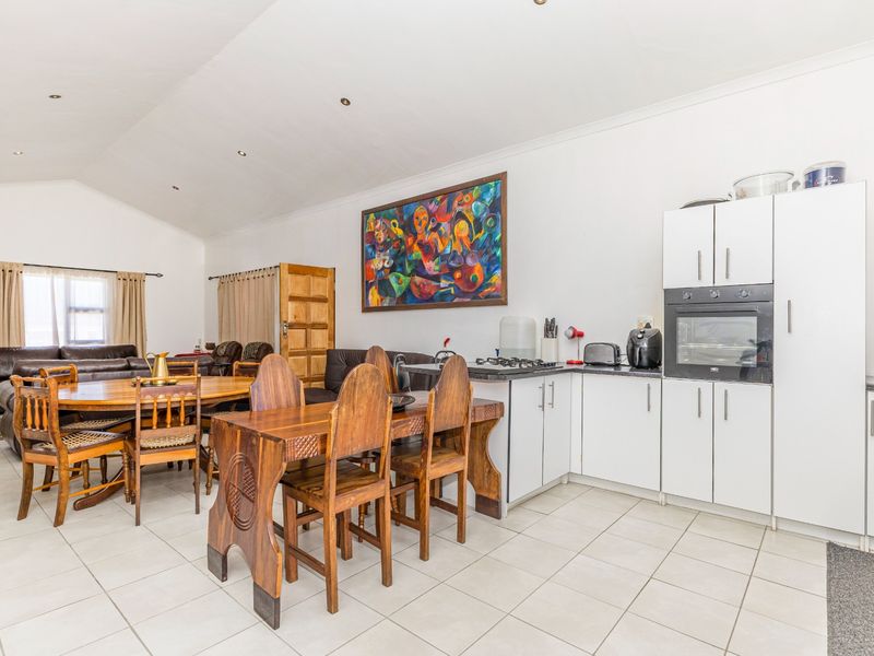 Spacious open-plan living and dining area featuring a functional kitchen with built-in oven, hob, and tiled flooring under a vaulted ceiling.