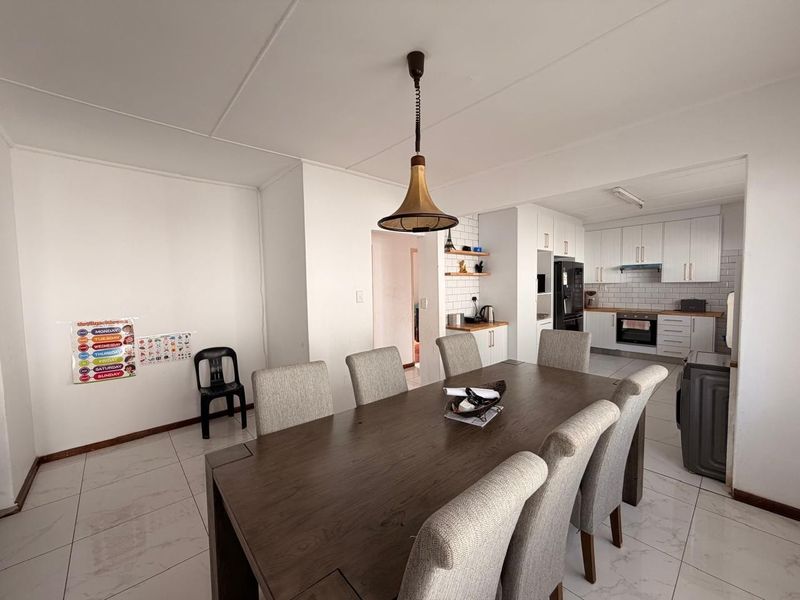 Open-plan dining area flowing into a modern kitchen featuring white cabinetry, subway tile backsplash, and integrated appliances.