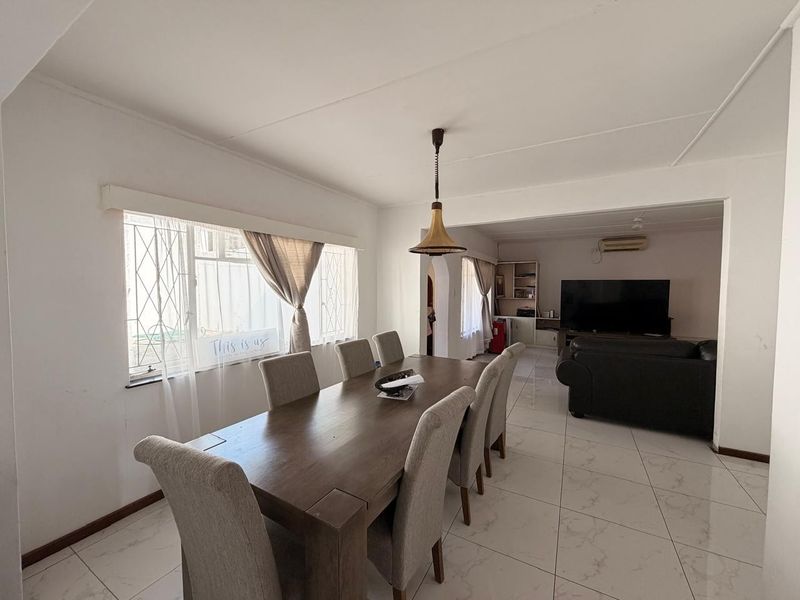 Open-plan dining and living area featuring tiled flooring, neutral walls, and an air conditioning unit, providing a functional and connected living space.