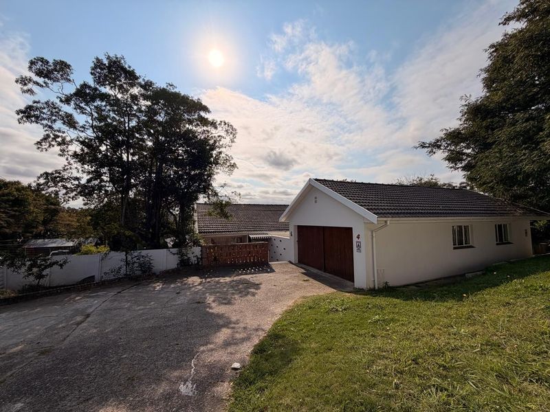Front exterior view of the property featuring a concrete driveway, double garage with timber doors, and established garden surroundings.