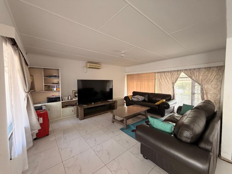 Spacious living room featuring light-colored tiled flooring, a built-in shelving unit, and a wall-mounted split-system air conditioner.