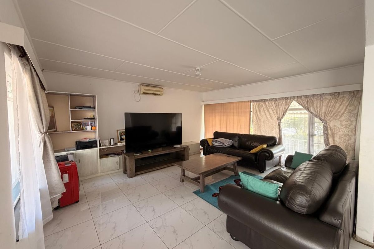 Spacious living room featuring light-colored tiled flooring, a built-in shelving unit, and a wall-mounted split-system air conditioner.