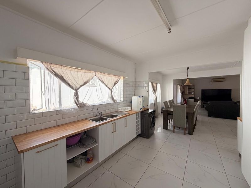 Open plan kitchen and dining area featuring white cabinetry, subway tile backsplash, butcher block countertops, and modern porcelain floor tiles.