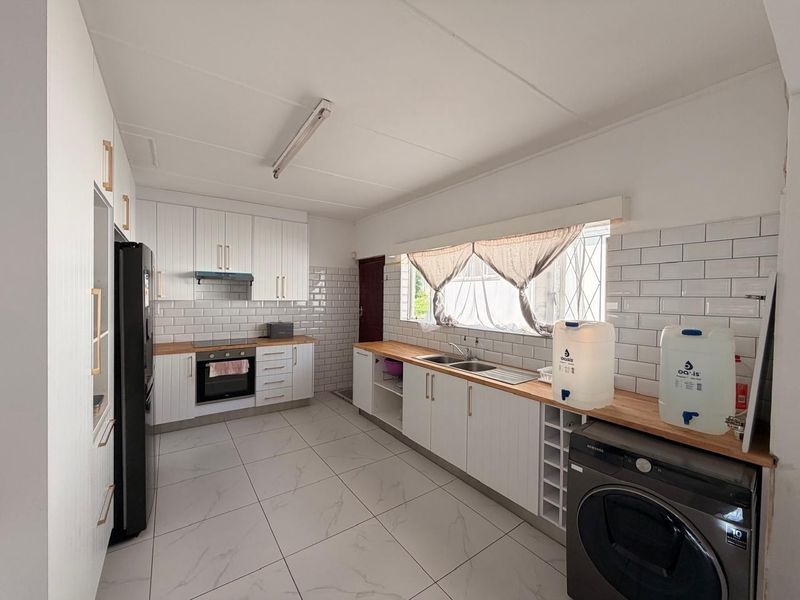 A bright, functional kitchen featuring white cabinetry, subway tile backsplash, wooden countertops, and modern floor tiles with integrated oven and extractor fan.
