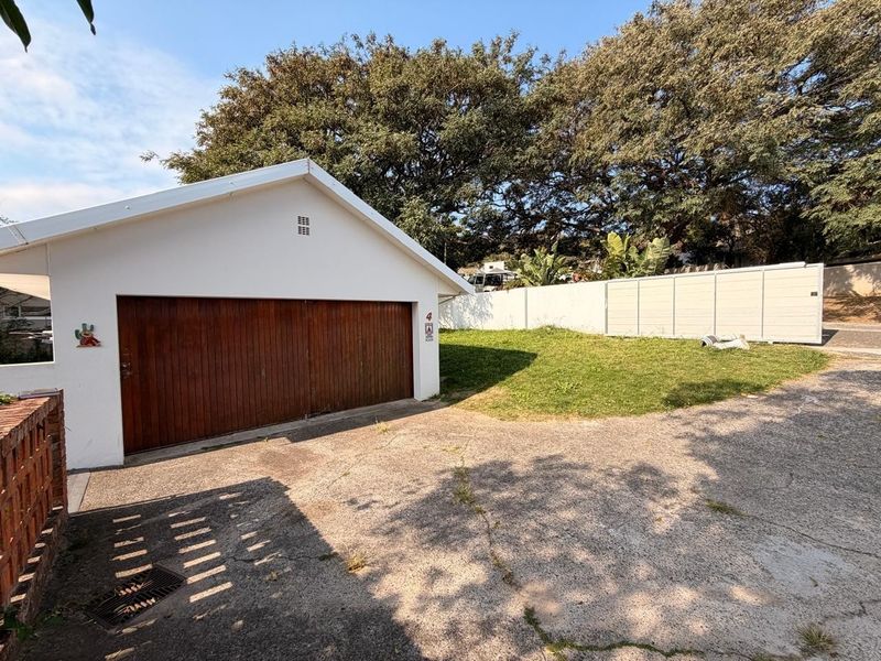 Exterior view of a detached garage featuring a wooden door, concrete driveway, and surrounding boundary wall.