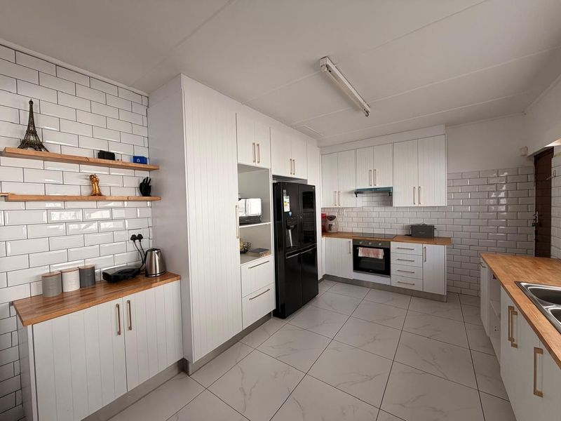 Modern kitchen featuring white cabinetry, subway tile backsplash, wooden countertops, and integrated appliances with large format floor tiles.
