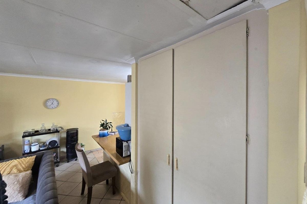 Living area featuring tiled flooring and a built-in cupboard, showing visible signs of ceiling damage and water staining.