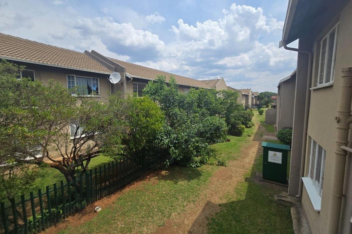 View of the rear exterior of the apartment complex, featuring communal garden spaces, tiled roofing, and established landscaping between building blocks.