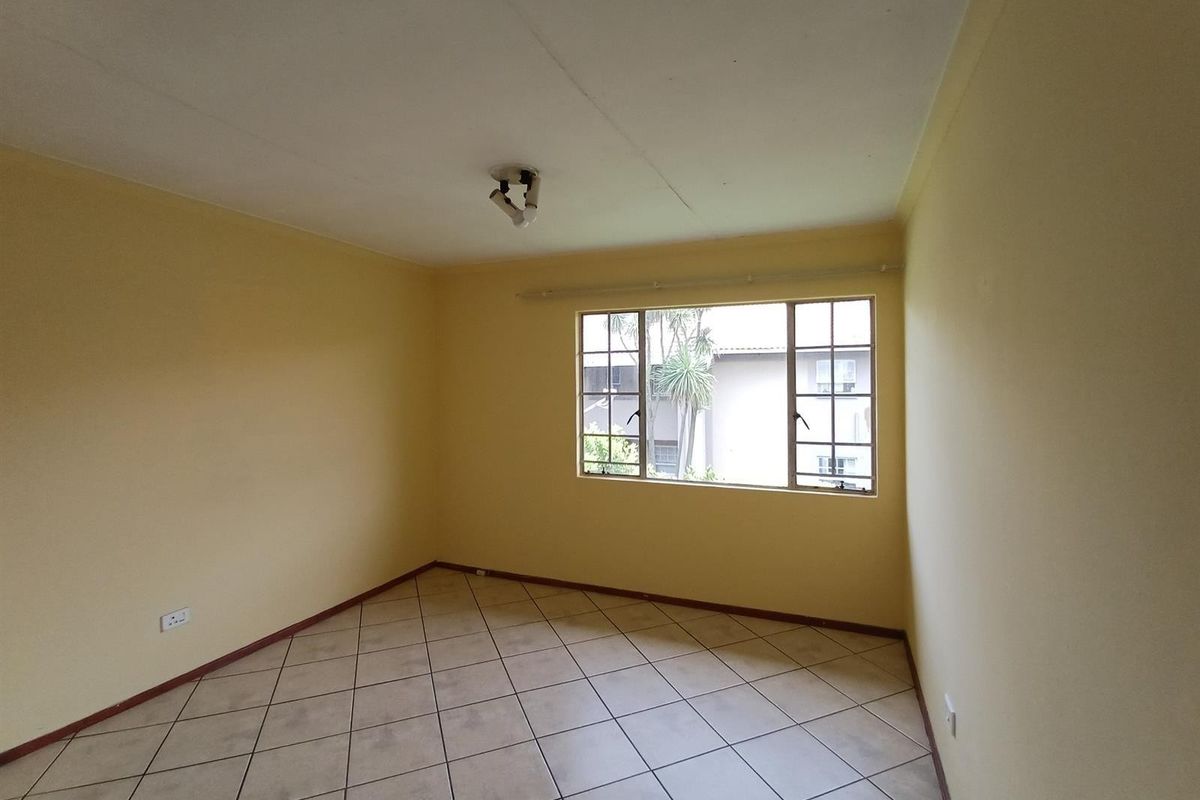 A vacant bedroom featuring neutral yellow walls, tiled flooring, and a large window providing natural light and a view of the complex exterior.