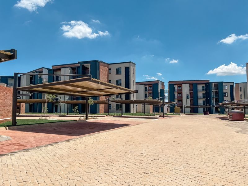 Exterior view of an apartment complex featuring paved driveways and covered parking bays under a clear blue sky.