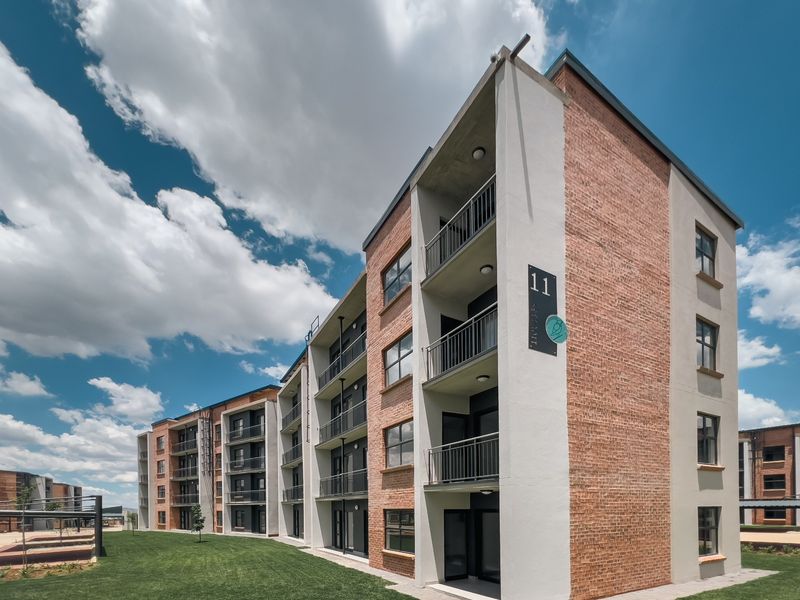 Modern multi-story apartment building featuring a classic brick facade, private balconies with metal railings, and well-maintained surrounding lawn areas.