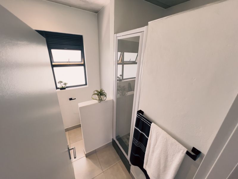A clean, modern bathroom featuring a shower enclosure, tiled flooring, and a functional window for natural light.