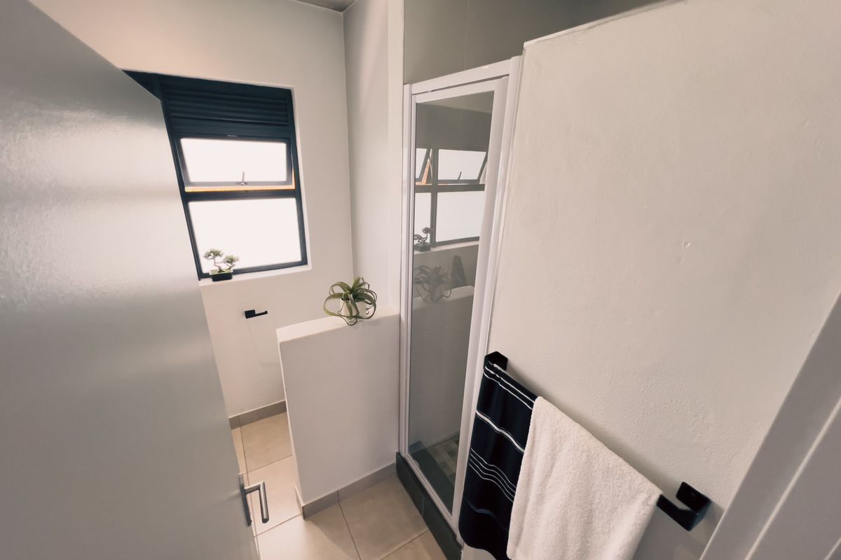 A clean, modern bathroom featuring a shower enclosure, tiled flooring, and a functional window for natural light.