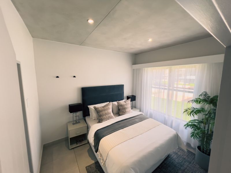 A well-lit bedroom featuring neutral tiled flooring, recessed ceiling lighting, and a large window allowing for ample natural light.