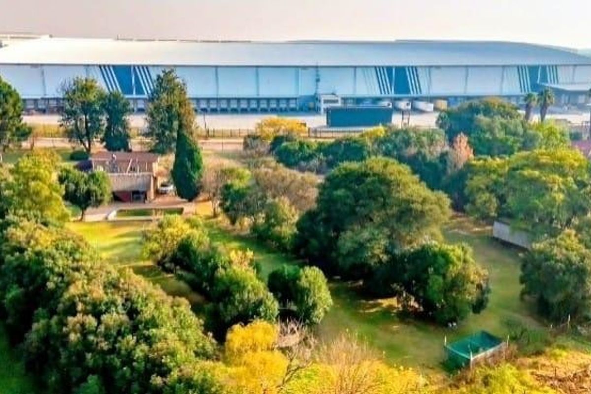 Aerial view of a large industrial warehouse facility featuring multiple loading docks, surrounded by extensive landscaped grounds and mature trees.