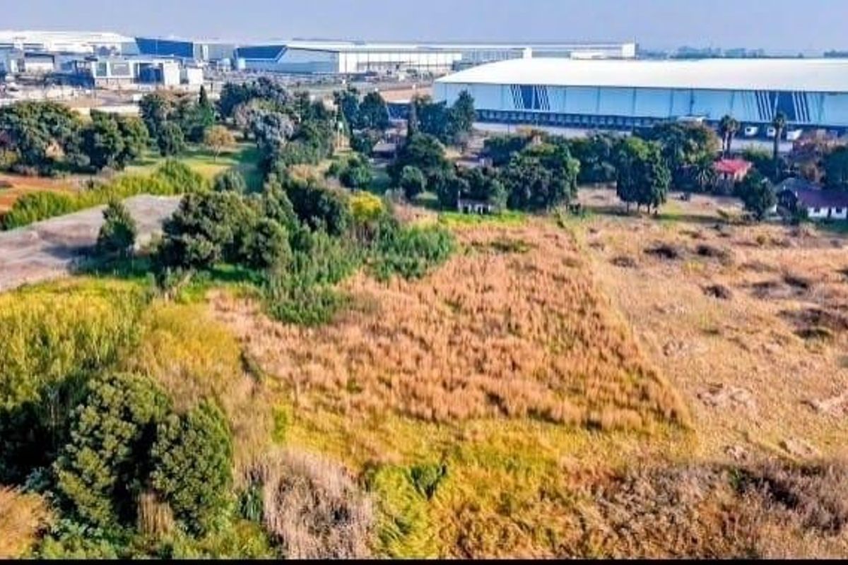 Aerial view of a large plot of undeveloped land situated in an industrial area, surrounded by established warehouse facilities.