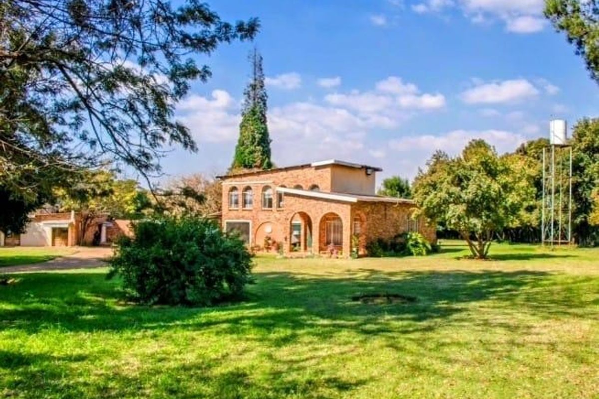 A view of the rear brick building facade featuring an arched porch, set within a spacious, well-maintained garden with an elevated water tower.