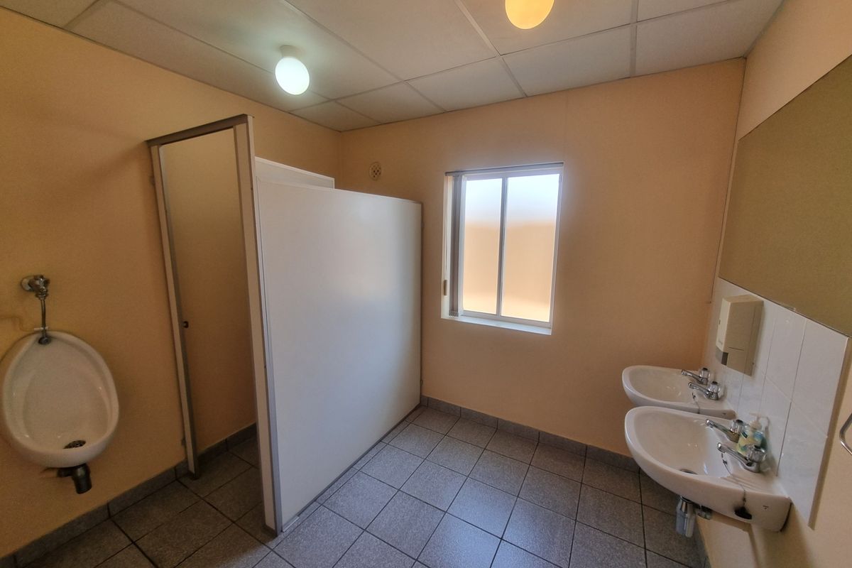 A functional office bathroom featuring tiled flooring, wall-mounted sinks, a urinal, and a privacy partition, providing essential facilities for a professional workspace.