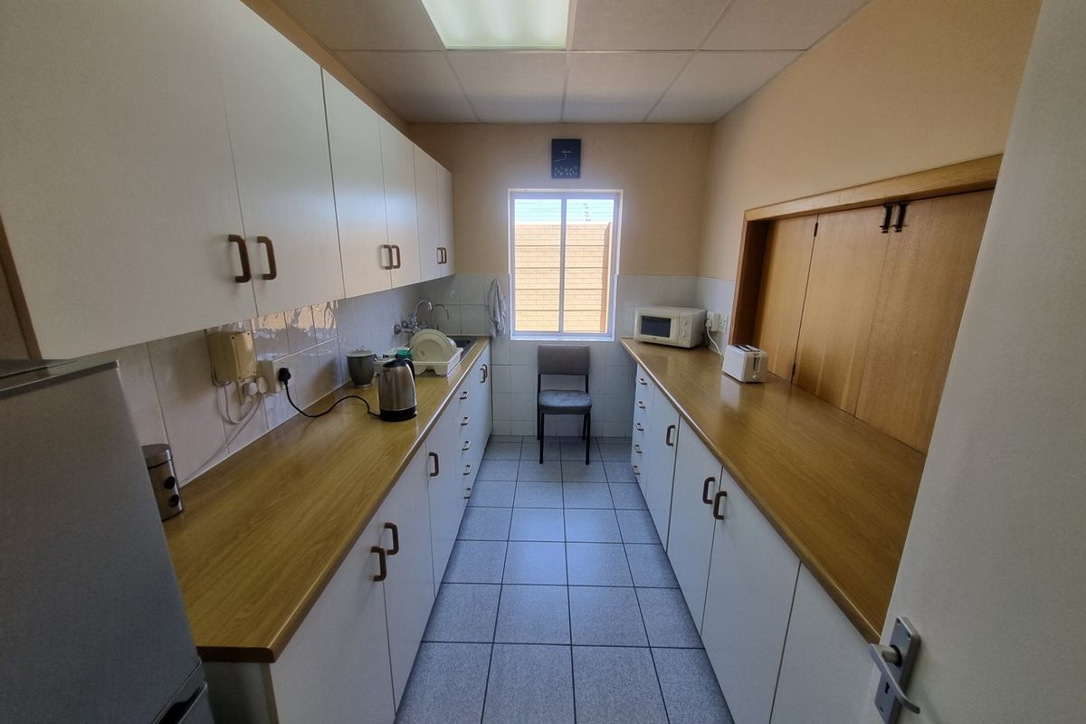 A functional office kitchenette featuring ample laminate counter space, white cabinetry, tiled flooring, and a drop ceiling with integrated lighting.