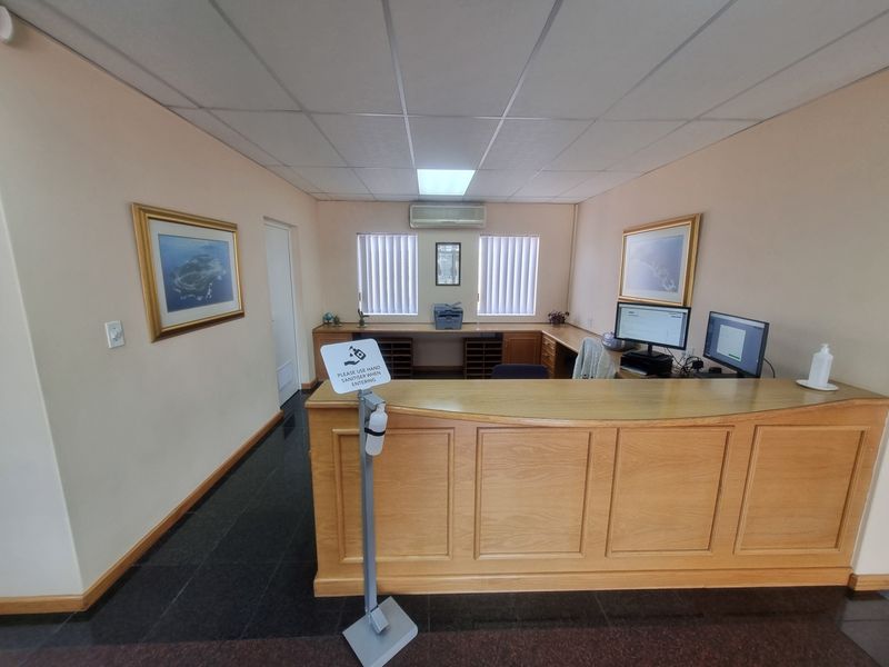 A professional office reception area featuring a built-in wooden desk, suspended ceiling, and split-system air conditioning unit.