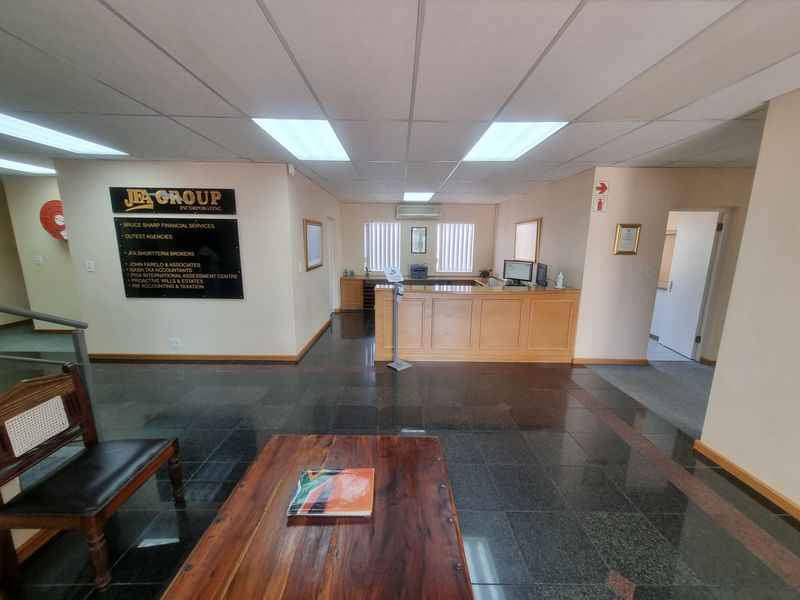 Professional office reception area featuring a built-in wooden reception desk, granite flooring, and integrated ceiling lighting.