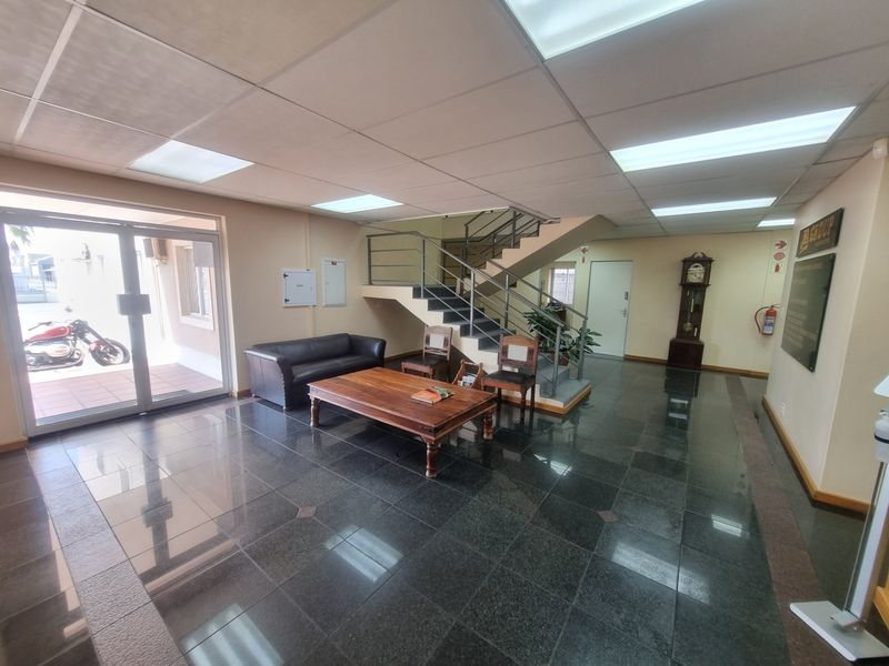 Spacious office reception area featuring polished granite flooring, a suspended ceiling with recessed lighting, and a central staircase leading to the upper level.