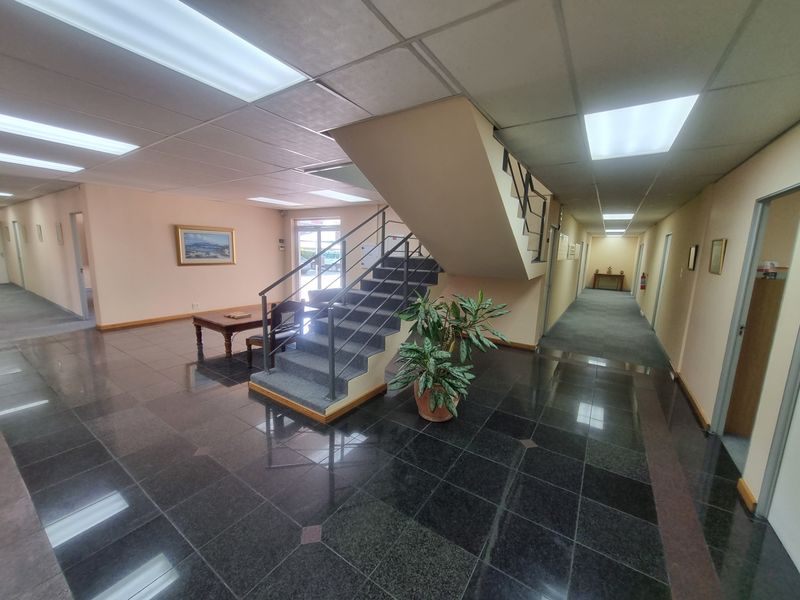 Spacious office building entrance foyer featuring a central staircase, polished granite flooring, and suspended ceiling with integrated lighting.