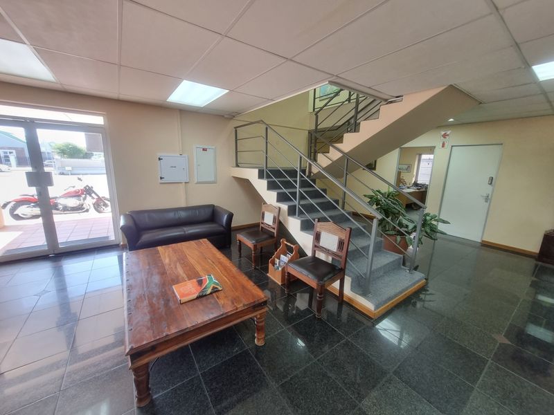 Spacious office building entrance foyer featuring polished tile flooring, a central metal staircase, and ample natural light from the glass entrance door.