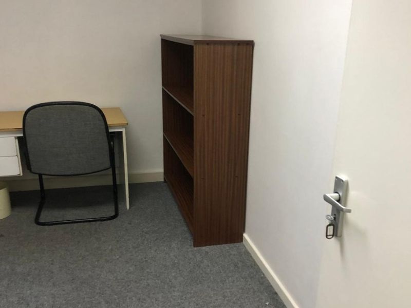 A compact office space featuring grey carpet flooring and a standard interior door with a lever handle.