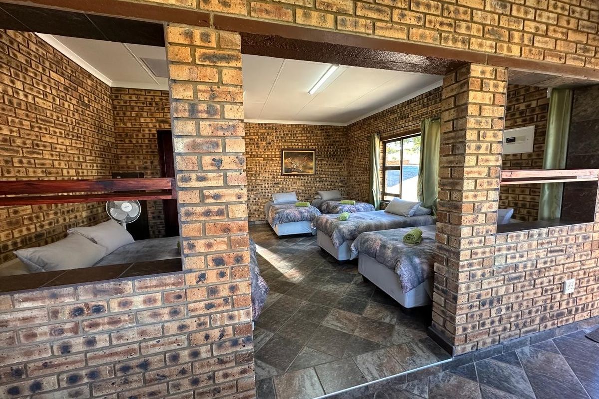 Spacious bedroom featuring exposed brick walls and tiled flooring, configured with multiple sleeping areas in an open-plan layout.