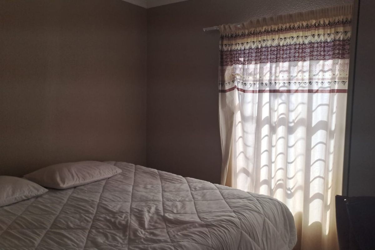 A standard bedroom featuring neutral wall paint and a window with a curtain rod.