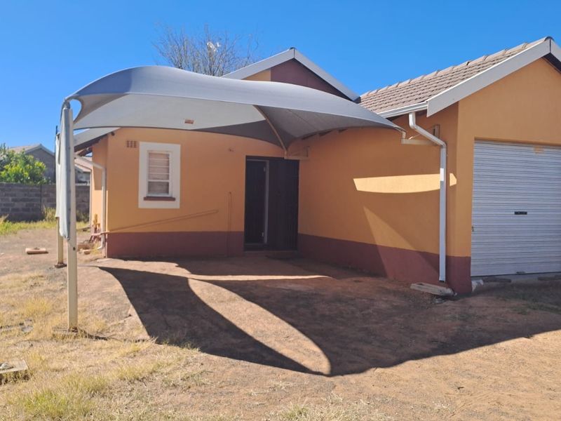 Rear view of the property featuring a shade sail, a single roller garage door, and a paved driveway area.