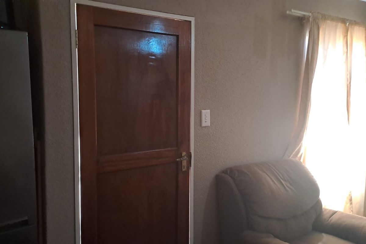 A view of a living room interior featuring a solid wooden door and window with curtain rod.