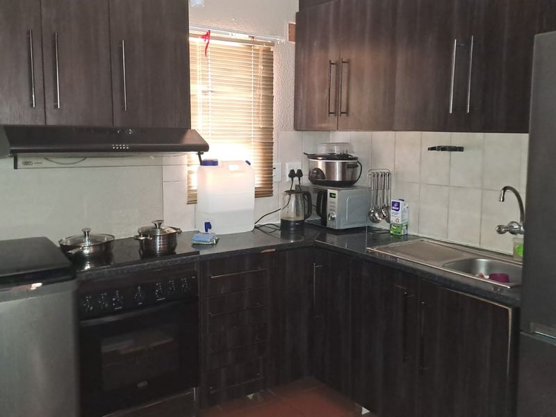 A functional kitchen featuring dark wood cabinetry, a built-in oven with extractor fan, stainless steel sink, and tiled backsplash.