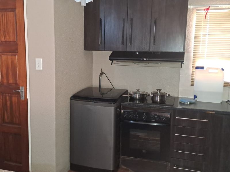 A compact kitchen featuring dark wood cabinetry, a built-in oven with hob, extractor fan, and a solid wood door.