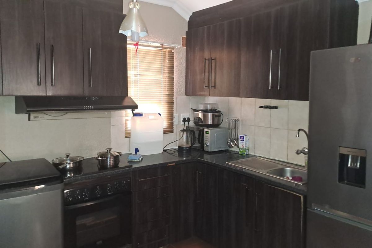 A functional kitchen featuring dark wood cabinetry, granite countertops, a built-in oven with extractor fan, and a stainless steel sink.
