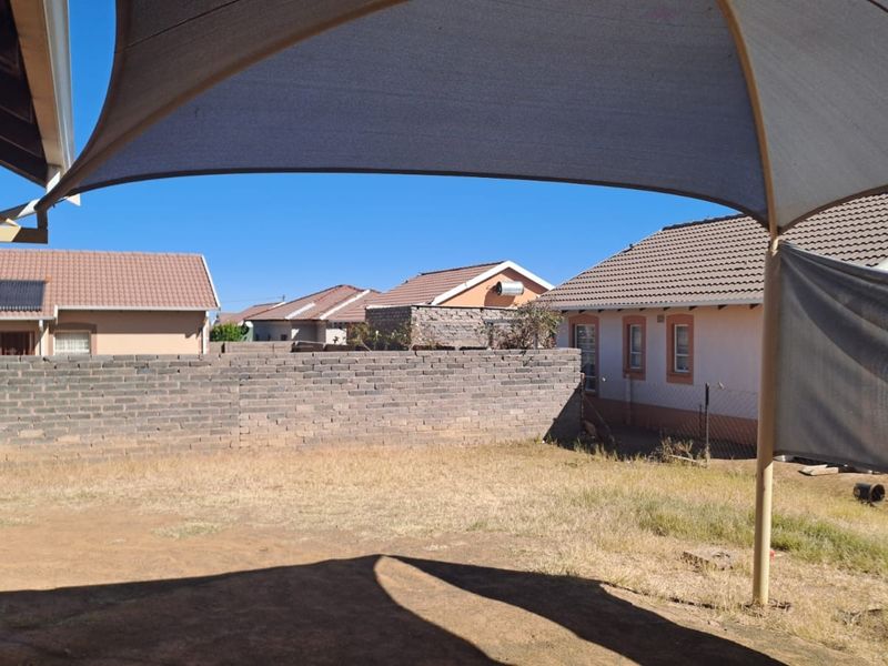 Rear yard area featuring a shade sail, brick boundary wall, and views of neighboring residential properties.