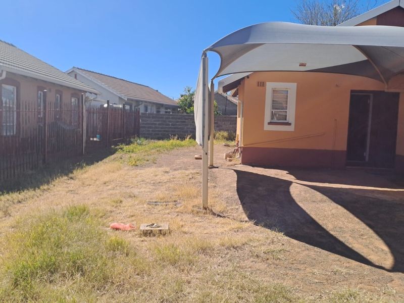 Rear exterior view of the property featuring a shade sail, metal perimeter fencing, and a garden area requiring maintenance.