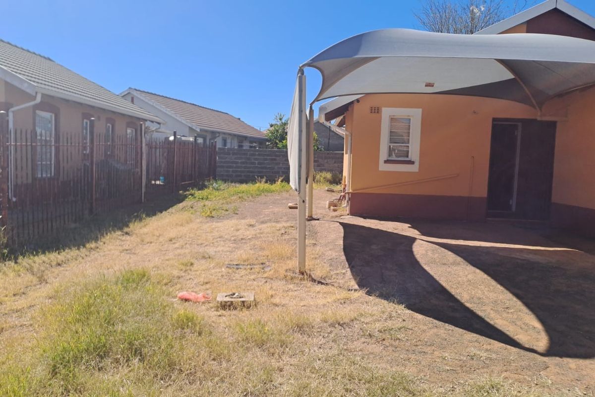 Rear exterior view of the property featuring a shade sail, metal perimeter fencing, and a garden area requiring maintenance.