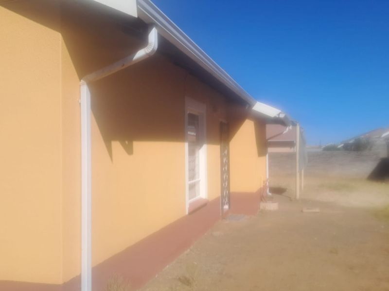 A view of the rear exterior of the house featuring yellow painted walls, guttering, and a security gate leading to an unlandscaped yard.