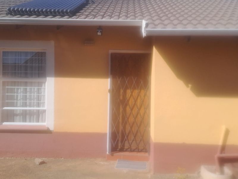 Rear exterior view of the house featuring a tiled roof with a solar water heater, a security gate, and painted exterior walls.