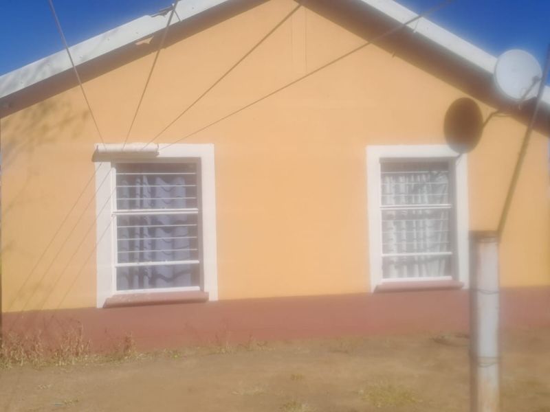 A view of the rear exterior facade of the house, featuring painted walls, security bars on windows, and a satellite dish installation.