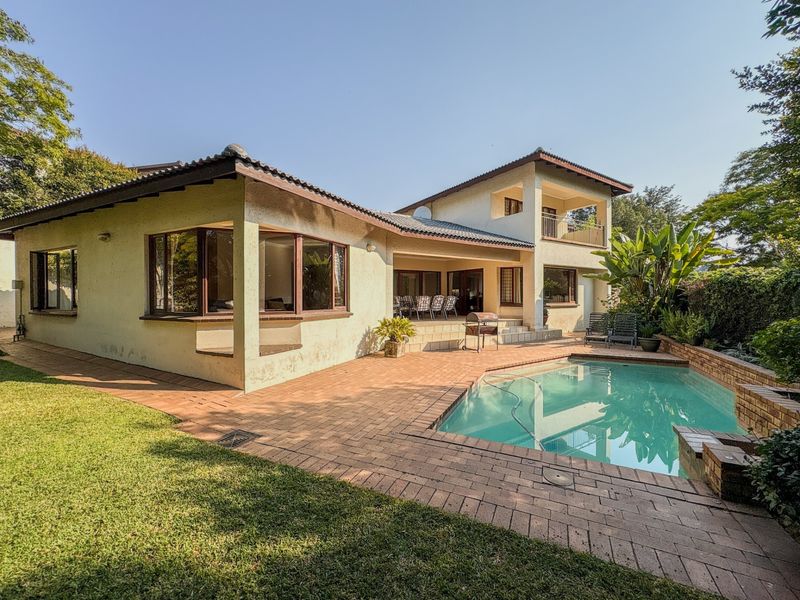 Rear view of the property featuring a swimming pool, brick paved patio area, and a two-story building structure with a balcony.