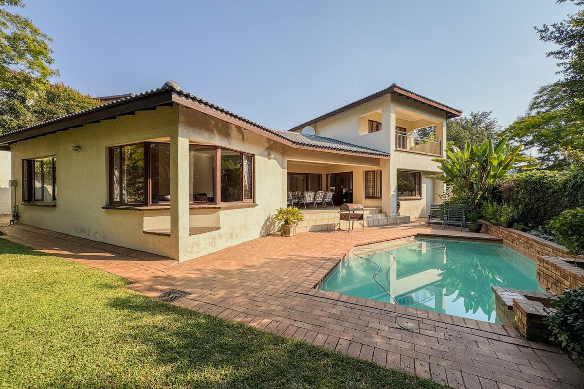 Rear view of the property featuring a swimming pool, brick paved patio area, and a two-story building structure with a balcony.